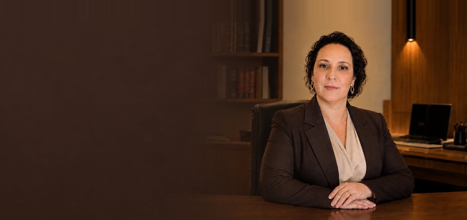 Adriana Monteiro Aliote Cardoso, advogada previdenciária em Lins/SP, sentada à mesa do escritório com estante de livros jurídicos ao fundo